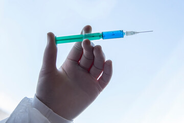 Doctor wearing surgical gloves holding a needle or syringe for injection with a blue liquid against white blue background.
