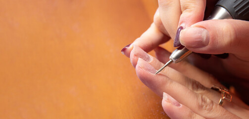 Grinding the skin near the finger nail with a thin cutter head. Independent home hand care. Space for the text. Selective focus.