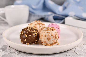 Colorful small cake balls glazed with white, pink and brown chocolate with sprinkles on white plate