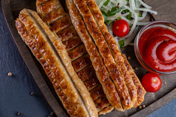 lula kebab made of chicken on a wooden board with pickled onions, chili peppers and cherry tomatoes on a dark background. photos with a small depth of field