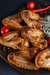 grilled on coals chicken wings on a wooden board with pickled onions, chili peppers and cherry tomatoes on a dark background. photos with a small depth of field, top view