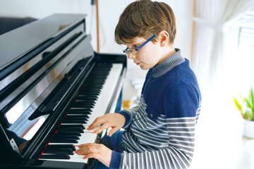 School boy with glasses playing piano in living room. Child having fun with learning to play music instrument. Talented kid during homeschooling corona virus lockdown. © Irina Schmidt