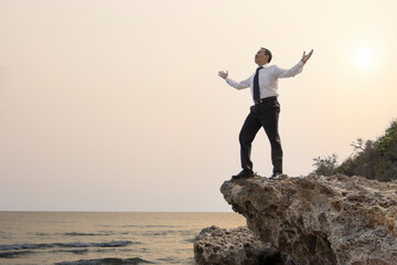 Fototapeta na wymiar Asian businessman standing on the cliff with two arms rising showing of great pleasure or happy satisfaction of enjoyment when business target reached or hard job finished