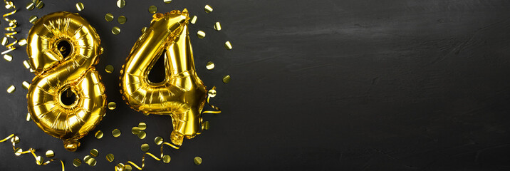 golden foil balloon number eighty four. Birthday or anniversary card with the inscription 84. Black concrete background. Anniversary celebration. Banner.