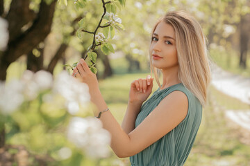 Young beautiful blonde woman in green dress stay at blooming garden