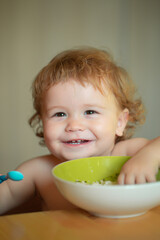 Launching child eat. Kid baby eat soup in the kitchen with dishes and spoon. Funny child face closeup.