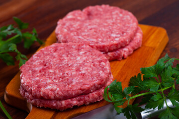 Raw meat burger cutlet with greens on wooden surface, nobody