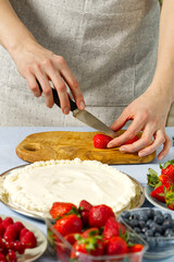 woman baker cuts strawberries for strawberry cake. Homemade strawberries cake made from meringue cake and cream with strawberries. home cooking concept