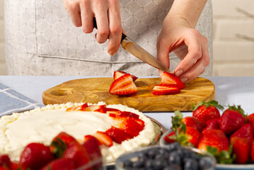 woman baker cuts strawberries for strawberry cake. Homemade strawberries cake made from meringue cake and cream with strawberries. home cooking concept