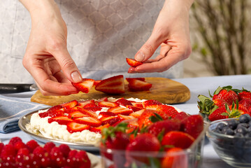 woman baker stacks strawberries on meringue strawberry cake base. Homemade strawberries cake made from meringue cake and cream with strawberries. home cooking concept