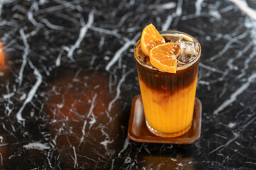Americano coffee mixed with orange juice in clear glass placed on a wooden tray on a black marble-cut white table.