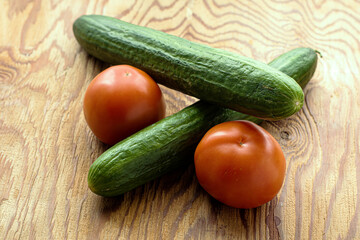 two cucumbers and two tomatoes on a wooden surface