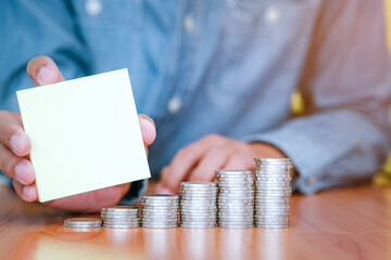 A businessman holding a blank note with coins stack placed on the front. Saving and investment concept for the future. copy space for text.