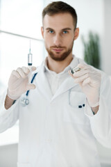 doctor in medical gloves and in a white coat with a vaccine in an ampoule and a syringe in his hand