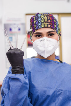 A portrait of a female dentist in her clinic with safety clothing and mask. She is showing hers tools. Retrato de una dentista en su clinica, con traje de bioseguridad.	mostrando sus herramientas.