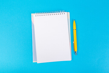 stack of school exercise books on blue background, spiral notepad with blank page and pen on table...