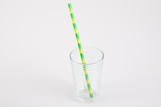 small glass transparent empty with green straw in carton recyclable cardboard on a grey table background