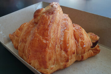 Freshly baked croissant on a takeaway paper plate in a pastry shop.