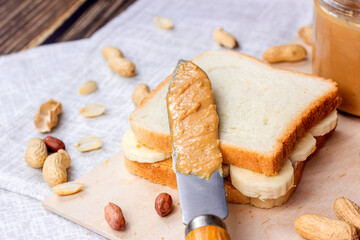 Homemade sandwich for breakfast with fresh crunchy peanut butter and bananas on light textile background.