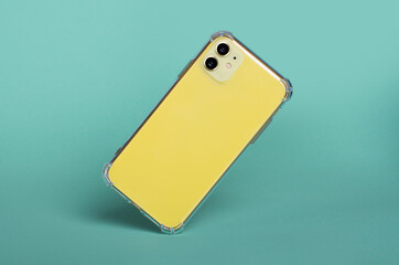 Yellow iPhone 11 in clear silicone case falls down isolated on green background back view. Phone case mockup