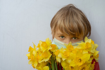 This is a portrait of a boy wearing a medical mask holding a bouquet of yellow flowers.