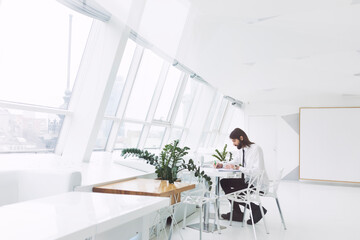 a business man in a white shirt and tie sits working with a laptop in a modern expensive office by the window
