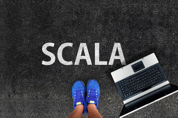 Scala programming language. man legs in sneakers standing next to laptop and word Scala