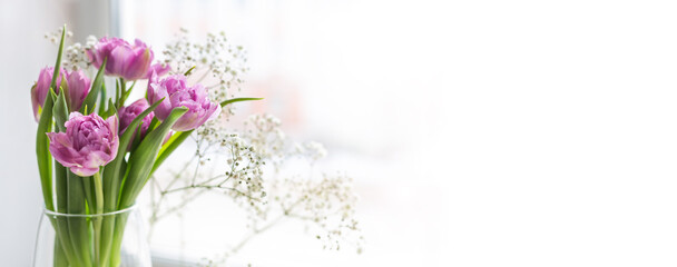 Bouquet of pink tulips and gypsophila in a glass vase by the window. Greeting card for mother's day, March 8 or wedding. Template for wedding invitation, banner with copy space. Spring morning.