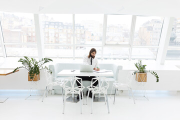 business man in a white shirt and tie sits at the table and works with documents and laptop in a modern office by the window

