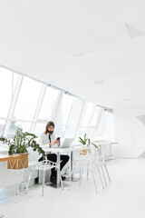 a business man in a white shirt and tie uses the phone and sits at a table with a laptop on the background of a white modern office by the window
