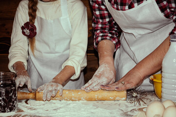 Mom teaches her daughter to knead the dough. Adult and little girls. Beautiful wooden background. Baking and cooking.