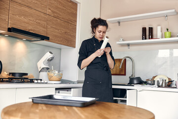 young beautiful mixed race woman spreads pastry paper on a dish in light modern kitchen