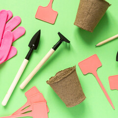 Flat lay of gardening supplies. Tools, peat pots, gloves and seedling plates on green background,...