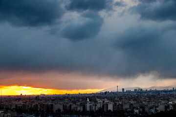 Fototapeta premium Tehran-Iran skyline at a moody sunset after a heavy storm. with Milad tower and beautiful snow covered mountains and amazing clouds in the background.
