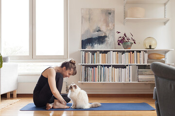 Woman and cat sitting on yogamat at home