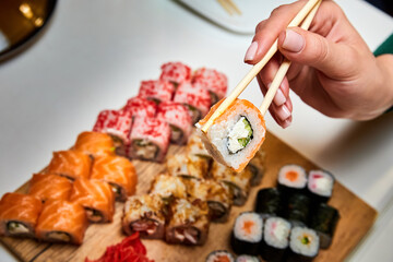 Girl holding chopsticks sushi roll on the background of a set of various sushi rolls. Close-up, selective focus.