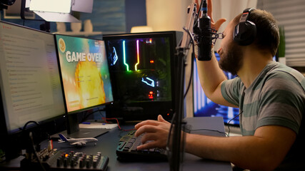 Game over for streamer playing space shooter video games using professional RGB keyboard and mouse. Pro gamer talking into microphone on streaming chat during online tournament