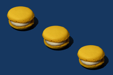 Food pattern made of bright yellow macarons with creamy white filling against royal blue background. Minimal aesthetic dessert concept. Summer composition.