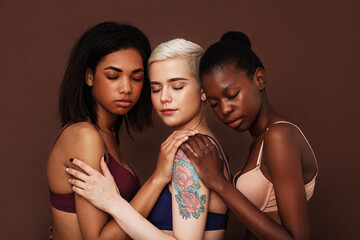 Three diverse women in bras standing with closed eyes over brown background - obrazy, fototapety, plakaty