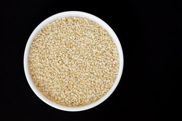 sesame seeds in bowl isolated on black background, top view