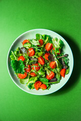 Healthy fresh salad of vegetable, tomato, spinach, arugula in a green plate on a green background. Food background for menu, recipe. Top view. salat with tomatoes cherry and green leafs. 