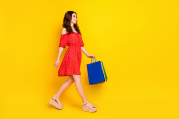 Full size profile photo of charming positive lady look empty space hold bags isolated on yellow color background