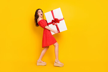 Full size profile photo of impressed girl arms hold big heavy giftbox open mouth isolated on yellow color background