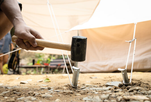 Hand of man holding a rubber mallet,hammering aluminium steel tent stakes pegs nail,fastening tent for camping,hit or beat anchor of the tent into the ground,hammer with rubber head, wooden handle