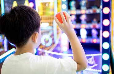 Kid boy playing a game of darts,holding a small plastic ball in his hands,aiming throwing at a...