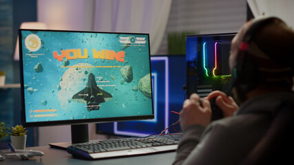 Winner gamer sitting on gaming chair playing space shooter video games with wireless controller. Pro cyber man streaming online video games for esport tournament on RGB powerful personal computer © DC Studio