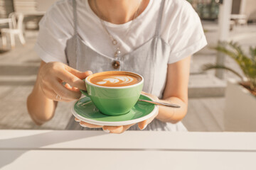 A happy woman drinks a fragrant fresh cappuccino coffee in an outdoor cafe on the terrace. The concept of leisure and a break for rest