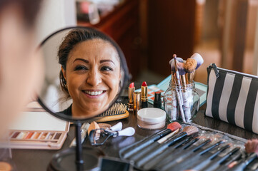 Reflection in a mirror of a woman putting on makeup and smiling