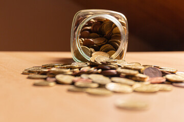 Half empty money jar with coins over the table. Front view. Save money concept banner.
