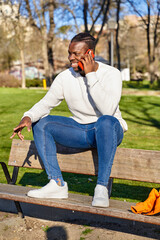 Happy black man talking on smart phone sitting in a park on a sunny day. 